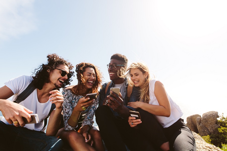 Young group of people sitting on top of mountain using smart phones and smiling