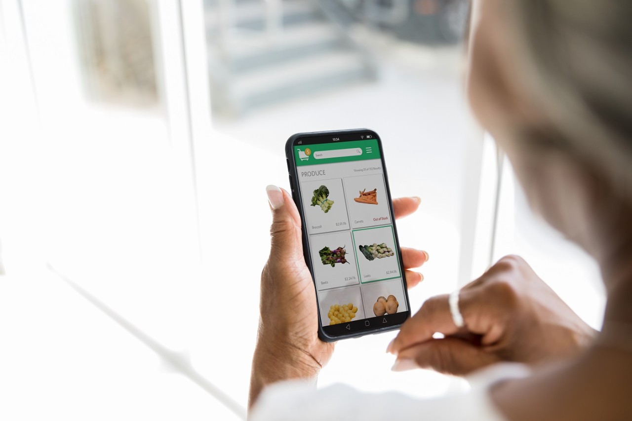 A woman uses a grocery delivery app on her smartphone. She is selecting fresh produce while using the app.