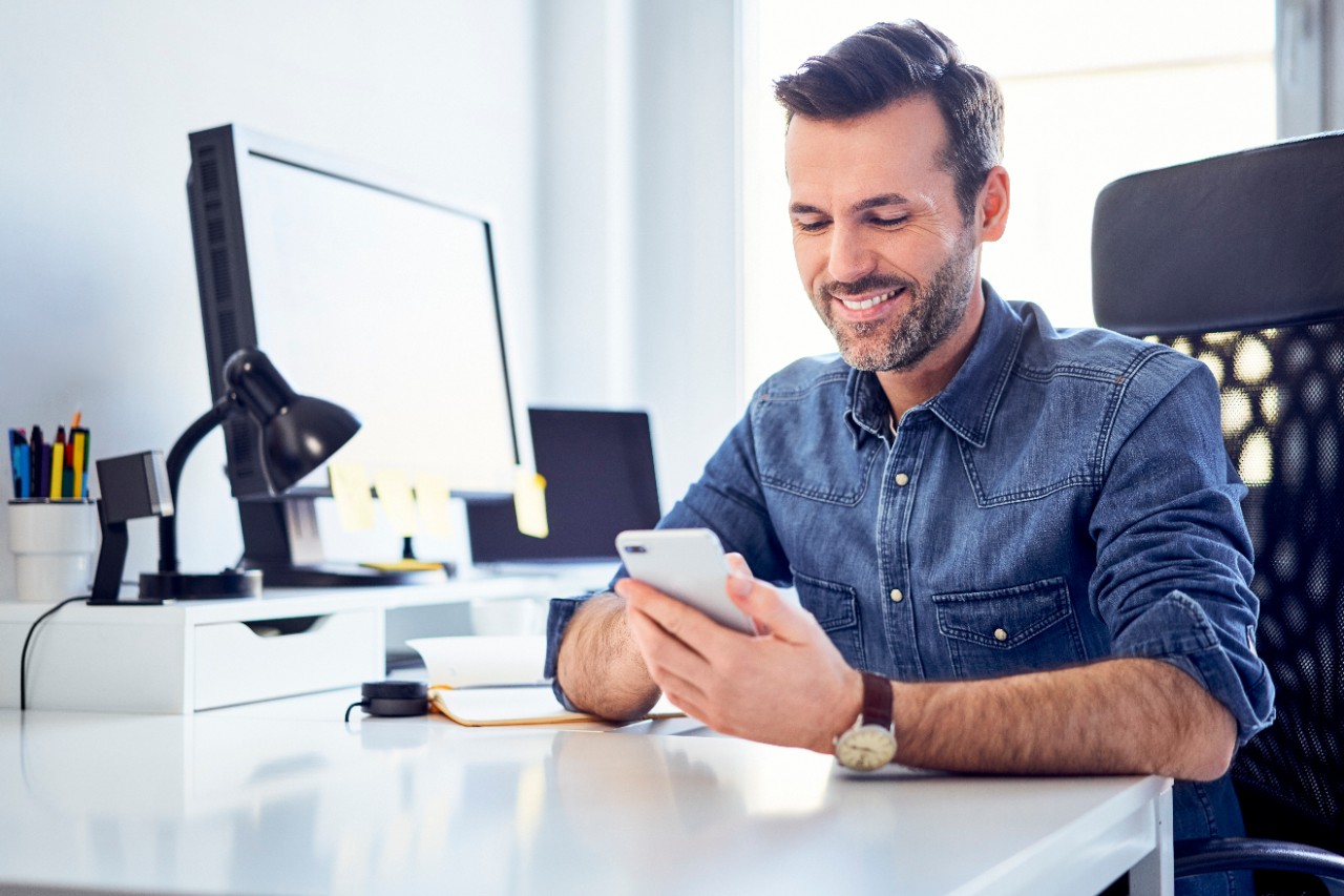 A man in office smiling at his cell phone