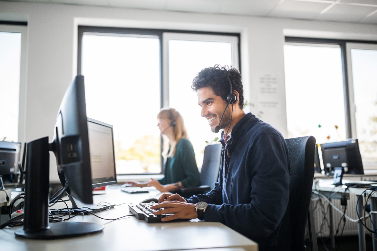 young man, call-center employee, wearing headphones sitting at a desk with a computer