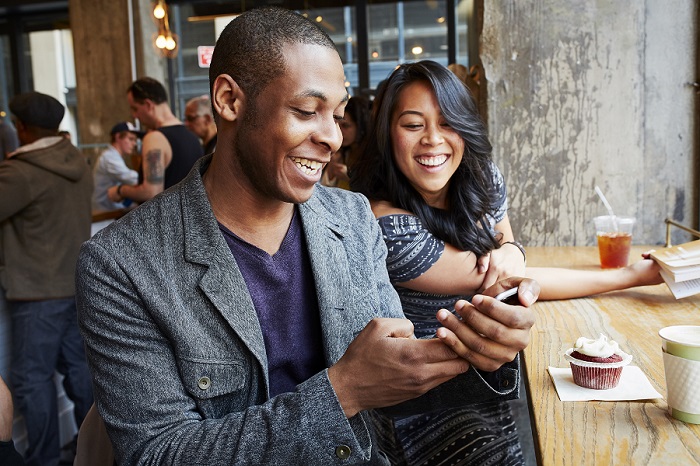 a man and a woman sitting in restaurant, smiling, looking at phone