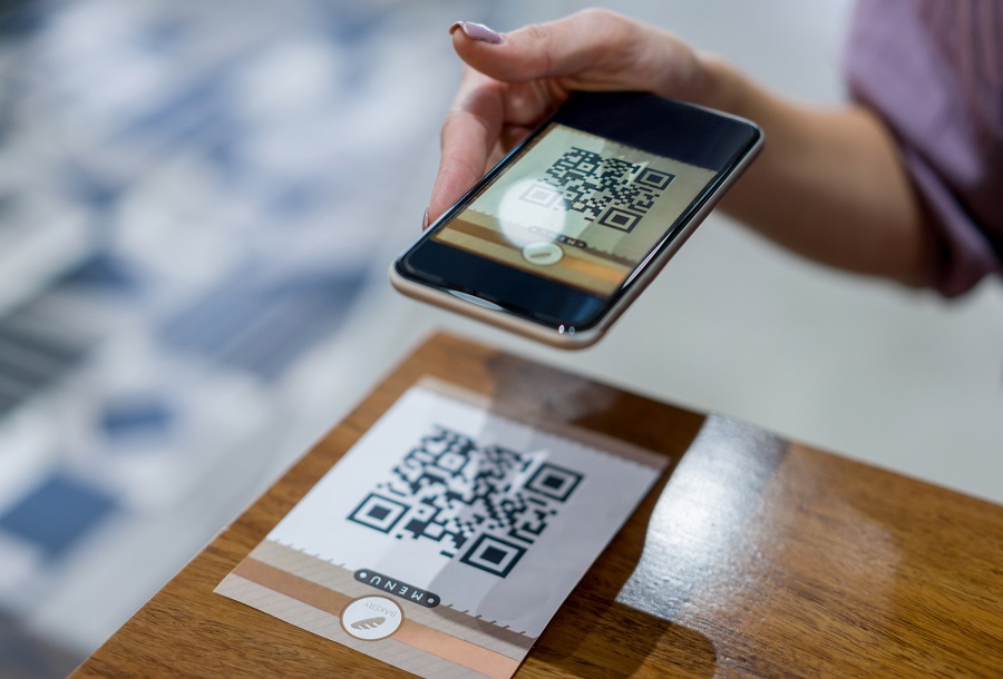 Close-up on a woman scanning a QR code to get the menu at a restaurant. **QR CODE WAS MADE FROM SCRATCH BY US**