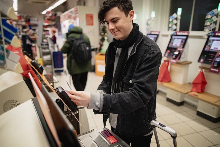 Young man smiling while using a self-service checkout machine in a supermarket