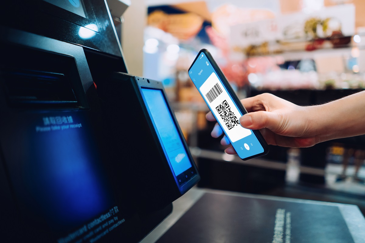 Close up of young woman shopping at a store, scanning QR code, making a quick and easy contactless payment via smartphone for her shopping at self-checkout kiosk. NFC technology, tap and go concept