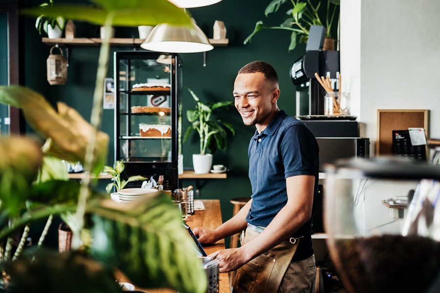 A smiling barista at work behind the counter at his busy cafe in the city.