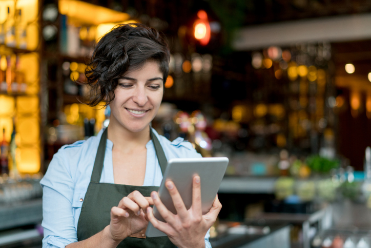 Happy waitress working at a restaurant and using app on a digital tablet