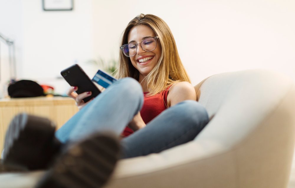 young female woman girl smiling in chair mobile ordering on her phone with her credit card