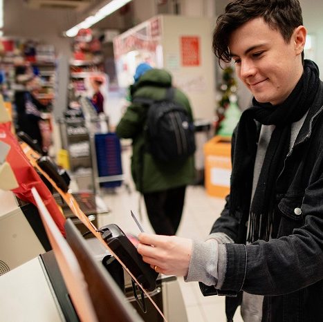 Young male adult smiling while using a self-service checkout machine while in a supermarket.