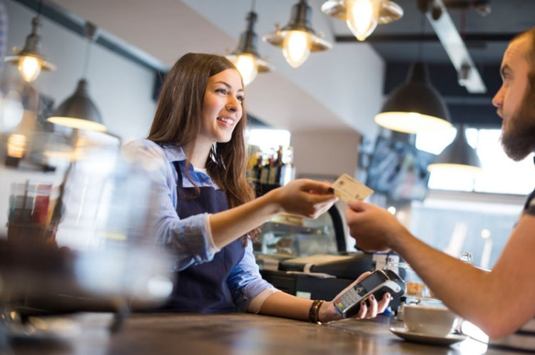 Barista employee takes credit card over counter from customer at cafe